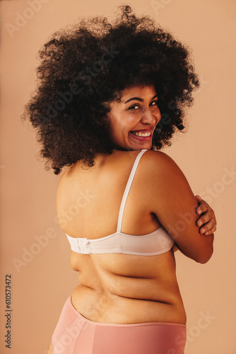 Smiling plus size woman embracing herself while wearing underwear