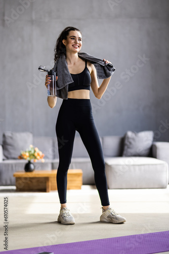 fitness, home and diet concept - smiling woman with bottle of water after exercising at home