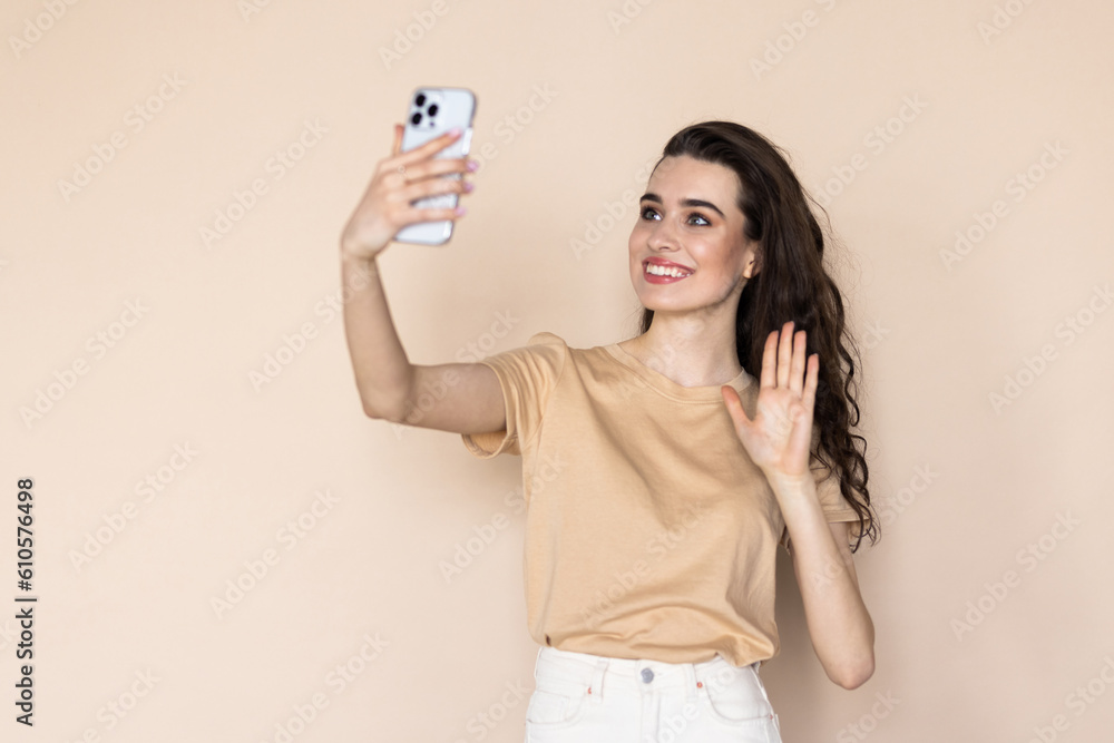 Young woman on a beige background waving her hand at the phone talking via video call Young woman on a beige background waving her hand at the phone talking via video call
