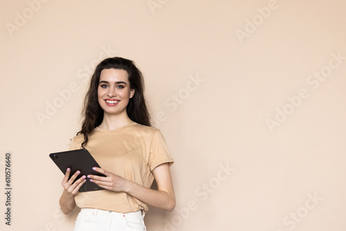 A young woman with a tablet in her hands on a beige background.