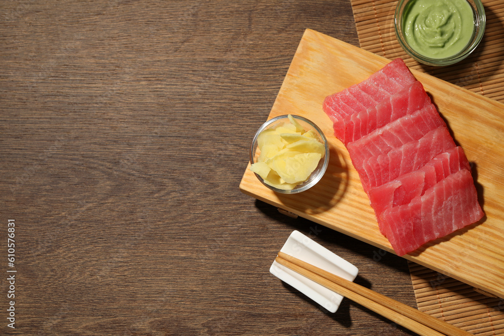 Tasty sashimi (pieces of fresh raw tuna) served with wasabi sauce and ginger slices on wooden table, top view. Space for text Tasty sashimi (pieces of fresh raw tuna) served with wasabi sauce and ginger slices on wooden table, top view. Space for text