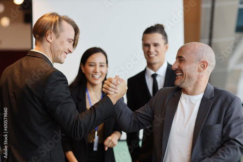 Young multiethnic collaborative process of professional businesspeople arm wrestling after new business contract signed with happy smiling face. Coworker and working together concept