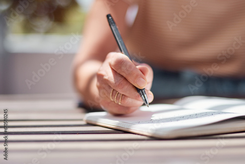 Hand, journal and book with a woman writer sitting outdoor in summer for inspiration as an author. Idea, planning and notebook with a female person using a pen to write in a planner or diary outside