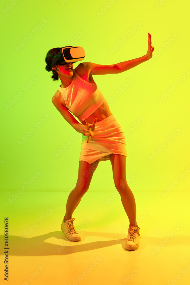 Girl wearing VR headset glasses playing virtual reality game over acid green and yellow background. Youth, virtual lifestyle of future