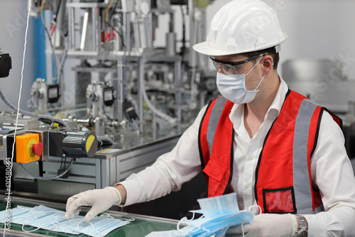 Caucasian mechanic technician maintenance or PPE inspecting quality of mask and medical face mask production line in factory, manufacturing industry and factory concept.