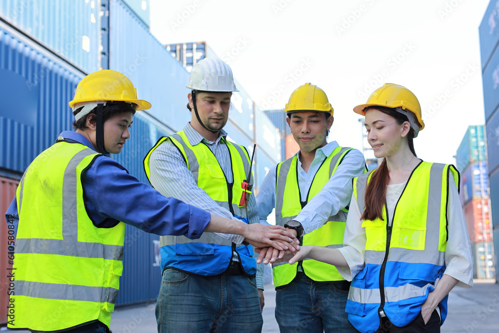 Group of multiethnic technician engineer and businessman in protective uniform with hardhat stand and stacking hands celebrate successful together or completed deal commitment at container cargo site Group of multiethnic technician engineer and businessman in protective uniform with hardhat stand and stacking hands celebrate successful together or completed deal commitment at container cargo site