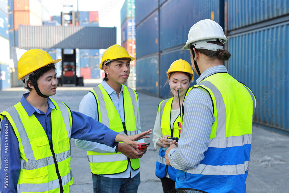 Group of multiethnic technician engineer in protective uniform standing and using computer, walkie talkie radio and tablet while.working together and controlling at container cargo site industrial Group of multiethnic technician engineer in protective uniform standing and using computer, walkie talkie radio and tablet while.working together and controlling at container cargo site industrial