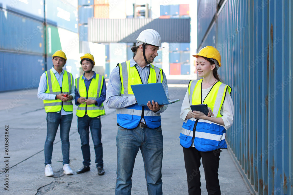 Group of multiethnic technician engineer in protective uniform standing and using computer, walkie talkie radio and tablet while.working together and controlling at container cargo site industrial Group of multiethnic technician engineer in protective uniform standing and using computer, walkie talkie radio and tablet while.working together and controlling at container cargo site industrial