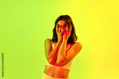 Portrait of tired girl, teenage, student with short hair grabbing face with hands over acid green, yellow background in neon light. Concept of human emotions photo