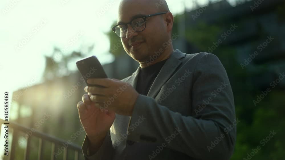 Confident businessman using smartphone to communication of business strolls and walking through a cityscape with towering buildings and lush trees blend of urban landscapes. Confident businessman using smartphone to communication of business strolls and walking through a cityscape with towering buildings and lush trees blend of urban landscapes.