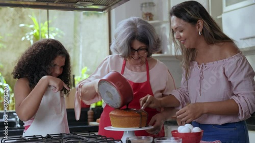 avó mãe e filha brasileiras na cozinha pondo cobertura no bolo que fizeram juntas para o dia das mães photo