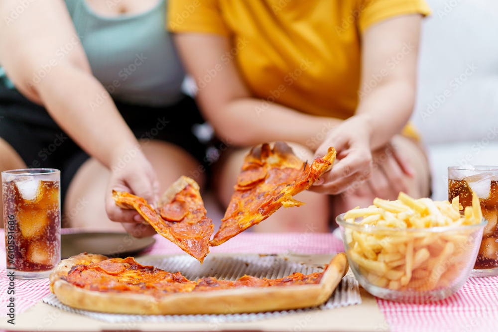 Happy oversize fat Asian women enjoy eating a pizza, hamburger, and French fry with drinking cola soda together. Unhealthy eating and unhealthy lifestyles concept. Happy oversize fat Asian women enjoy eating a pizza, hamburger, and French fry with drinking cola soda together. Unhealthy eating and unhealthy lifestyles concept.