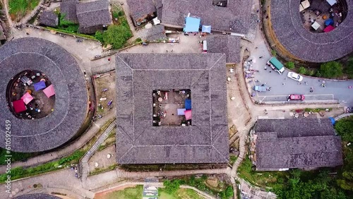 Drone shot zooms out of a square-shaped Unesco World Heritage Tulou Hakka. Traditional architecture with other Tulou houses on a mountain hill with people walking around, Fujian, China photo
