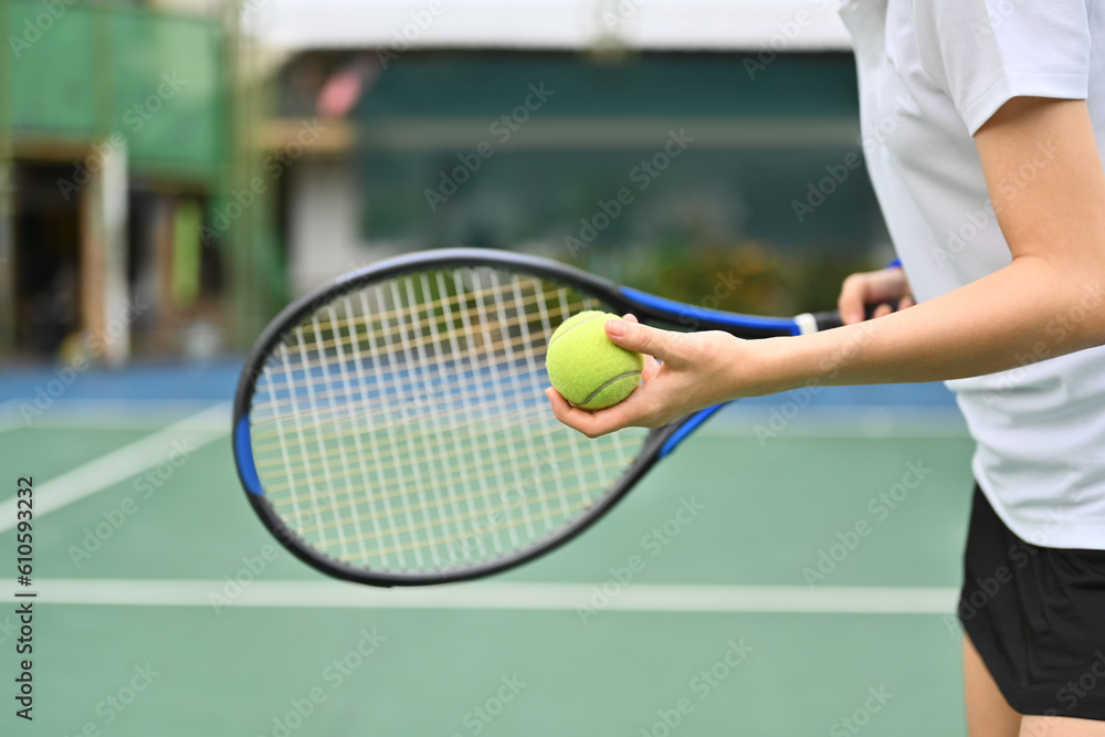 Sporty young woman preparing to serve tennis ball during match. Outdoor sports and healthy lifestyle concept