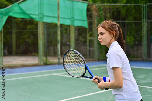 Focused female tennis player standing in ready position to receive a serve, practicing for competition on a court