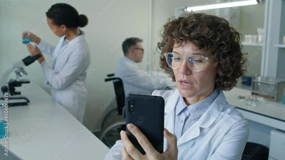 Medium closeup of Caucasian female chemist talking about research and showing test tube with liquid during video call in laboratory Medium closeup of Caucasian female chemist talking about research and showing test tube with liquid during video call in laboratory
