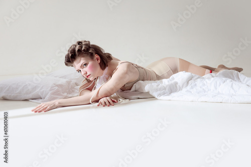 Pretty look. Beautiful  tender young girl with pink blusher on cheeks lying in retro lingerie on blanket against grey studio background