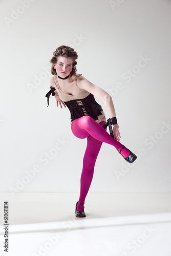 Portrait of young beautiful girl with blushing cheeks, wearing in black corset and pink tights, posing against grey studio background © Lustre Art Group 
