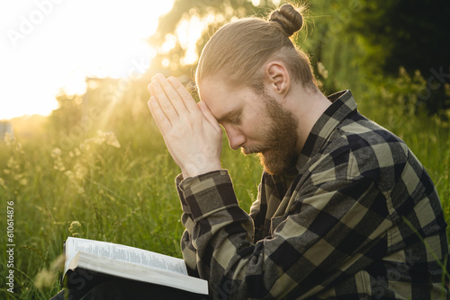 Man praying on the holy Bible in a field during sunset, male sitting with closed eyes, concept for faith, spirituality, and religion Fototapet