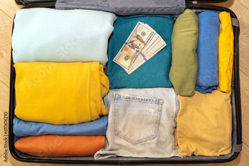 Top view of a suitcase filled with clothes and a stack of dollars. Preparations for travel, air travel, resort vacation. Freedom of movement, remote work.