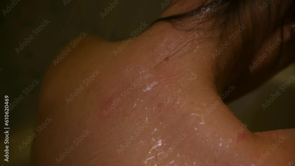 Close up of a person's neck and back under the jets of water in the shower. Close-up of a woman's body in the bathroom. A feminine back under streams of water. High quality 4k footage Close up of a person's neck and back under the jets of water in the shower. Close-up of a woman's body in the bathroom. A feminine back under streams of water. High quality 4k footage