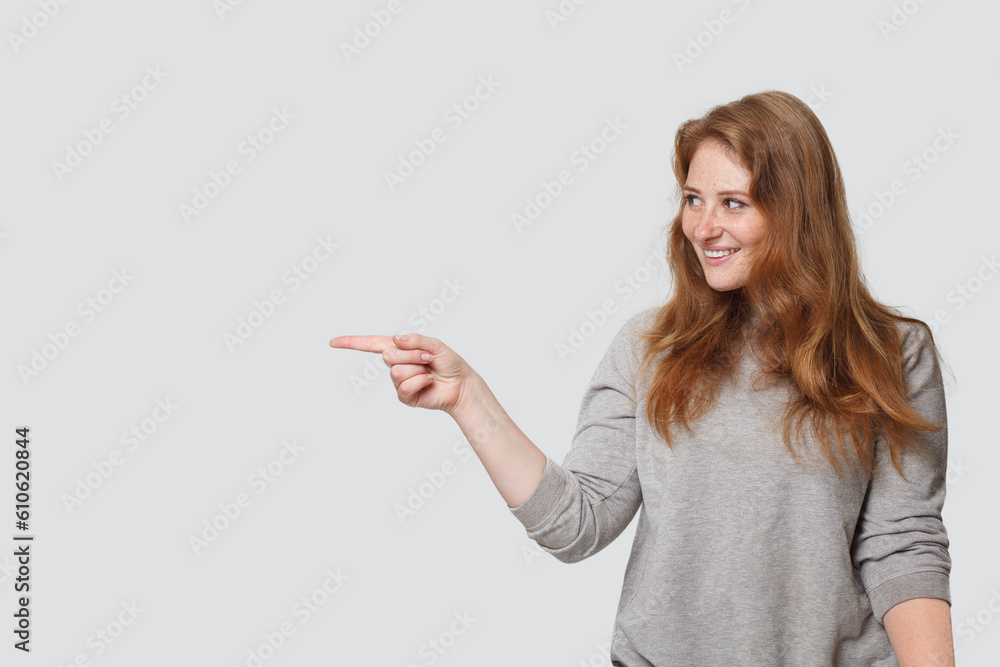 Pretty smiling woman pointing finger at copy space on white studio wall background Pretty smiling woman pointing finger at copy space on white studio wall background