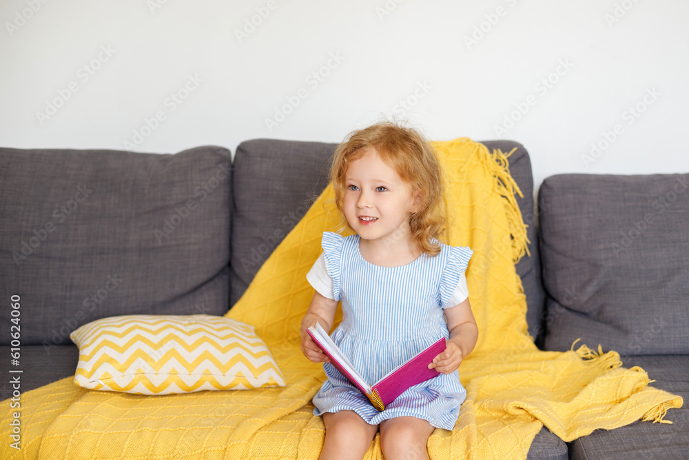 3-year-old girl sits at home on the couch with a pink glittery notebook 3-year-old girl sits at home on the couch with a pink glittery notebook