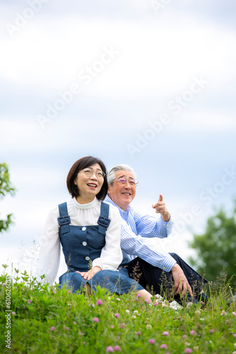 新緑の草原に座るミドルの日本人夫婦、公園のクローバー、芝生