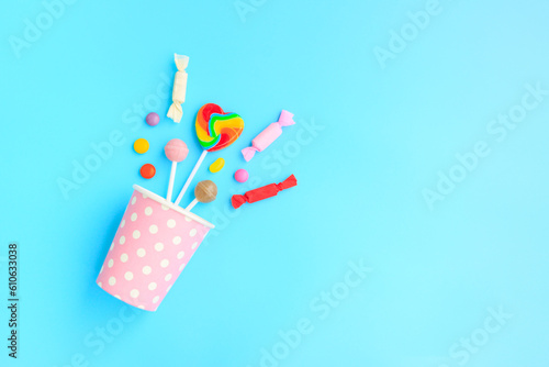 Different kinds of colorful lollipop and candy out of a pink paper cup with white dot on blue background, Various candies