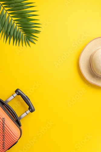 Dreaming of summer vacation. Vertical top view of a suitcase, beach accessories, sunhat, and palm leaf on a lively yellow background. Space available for text or advertisement