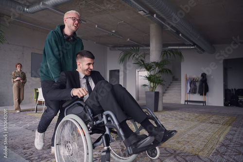 A young entrepreneur and his colleague, who is a person with a disability, fun together through a large, modern office, demonstrating the power of teamwork, inclusivity, and determination as they © .shock
