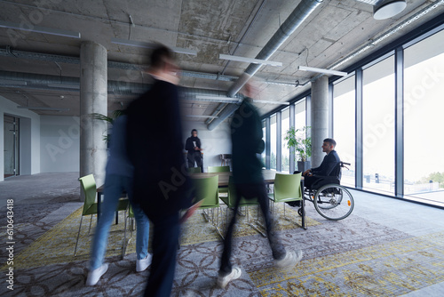 A businessman in a wheelchair sits at a table in a large, modern office, while his colleagues gather around, their steps blurred, symbolizing inclusivity, support, and unity in the face of challenges.