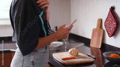 Young woman searching for recipe on her smartphone and beginning to cook