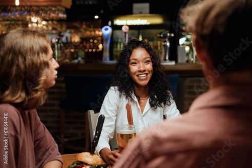 Happy young multiracial group of friends in casual clothing talking during dinner at restaurant