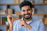 Young arab man with beard wearing casual clothes holding an invisible braces aligner and pointing at it, recommending this new treatment. Dental healthcare concept.