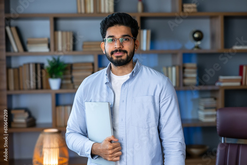 Smiling IT worker in blue shirt look at camera holding laptop at office. concept of remote and freelance work. millennial successful man in glasses