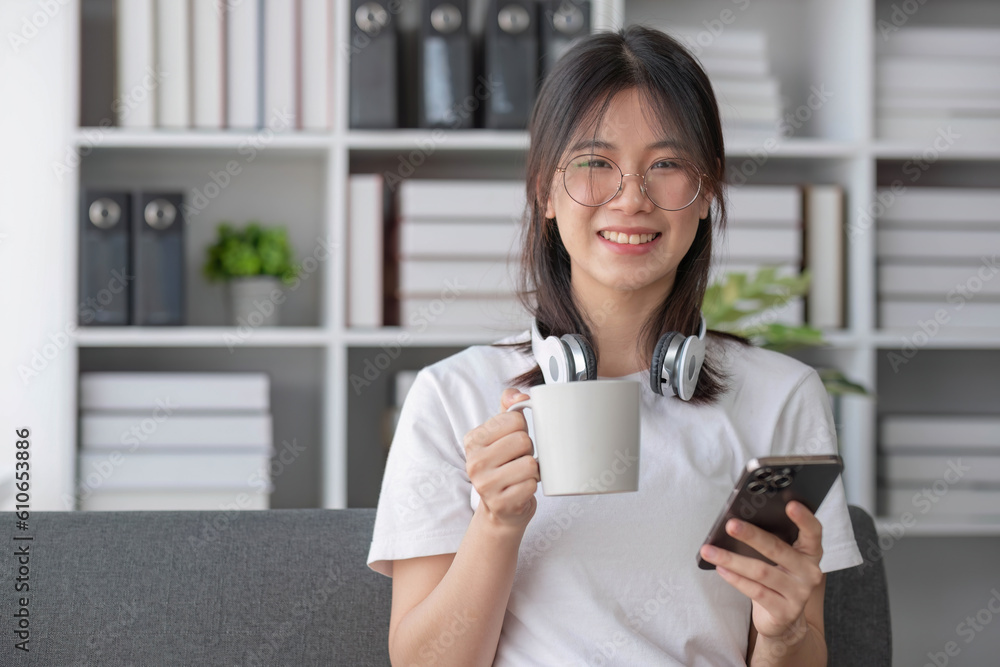 Attractive and happy young Asian female using her smartphone to scroll through social media while relaxing on her comfortable sofa in her living room. Attractive and happy young Asian female using her smartphone to scroll through social media while relaxing on her comfortable sofa in her living room.