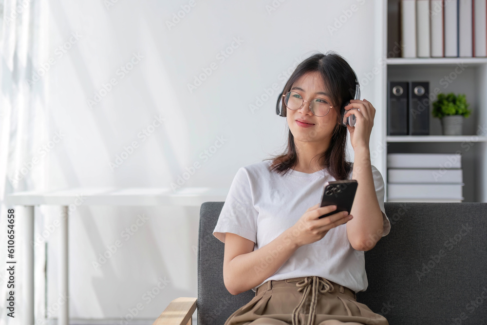 Attractive and happy young Asian female using her smartphone to scroll through social media while relaxing on her comfortable sofa in her living room. Attractive and happy young Asian female using her smartphone to scroll through social media while relaxing on her comfortable sofa in her living room.
