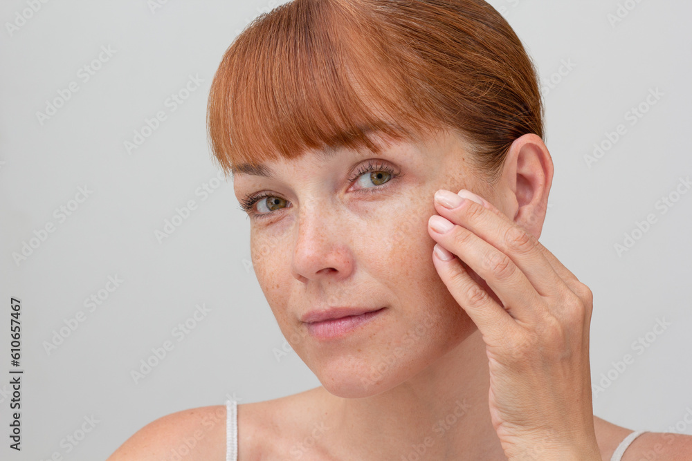 Portrait of cropped caucasian middle aged woman face with freckles touching skin by hand on white background looking at camera Portrait of cropped caucasian middle aged woman face with freckles touching skin by hand on white background looking at camera