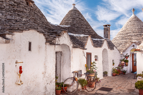 Trulli houses decorated with plants and flowers; a bunch of garlic and cherry tomatoes hanging on the whitewash wall. Alberobello, Bari, Italy