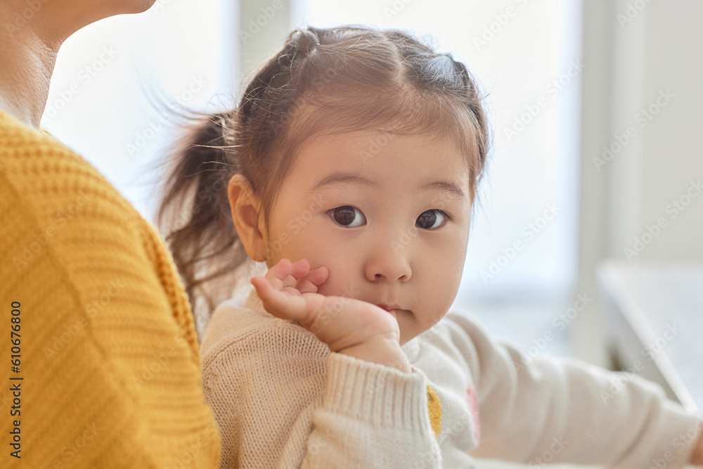 Portrait of Asian cute baby girl looking at camera while sitting on her mothers knees