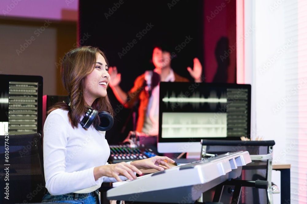 Fototapeta premium Asian producer woman in white shirt playing piano in sound studio with warm lighting background, Happy female music composer artist.