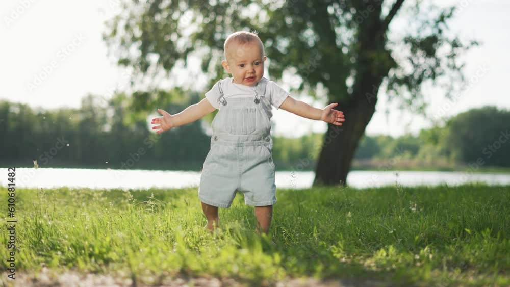 Happy baby takes first steps in nature.toddler walks on grass in park.Toddler steps on grass with his feet making first happy steps.Summer walk of toddler in park on grass. Baby first spring steps