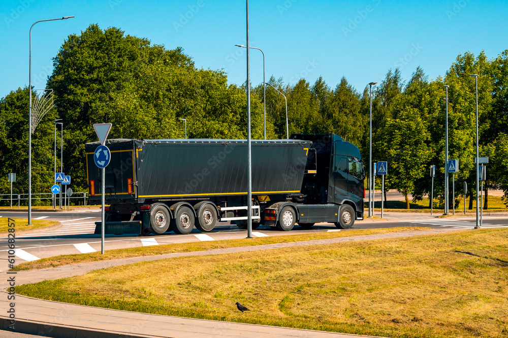 Big black dump truck maneuvering in the narrow pass of a landscaped roundabout