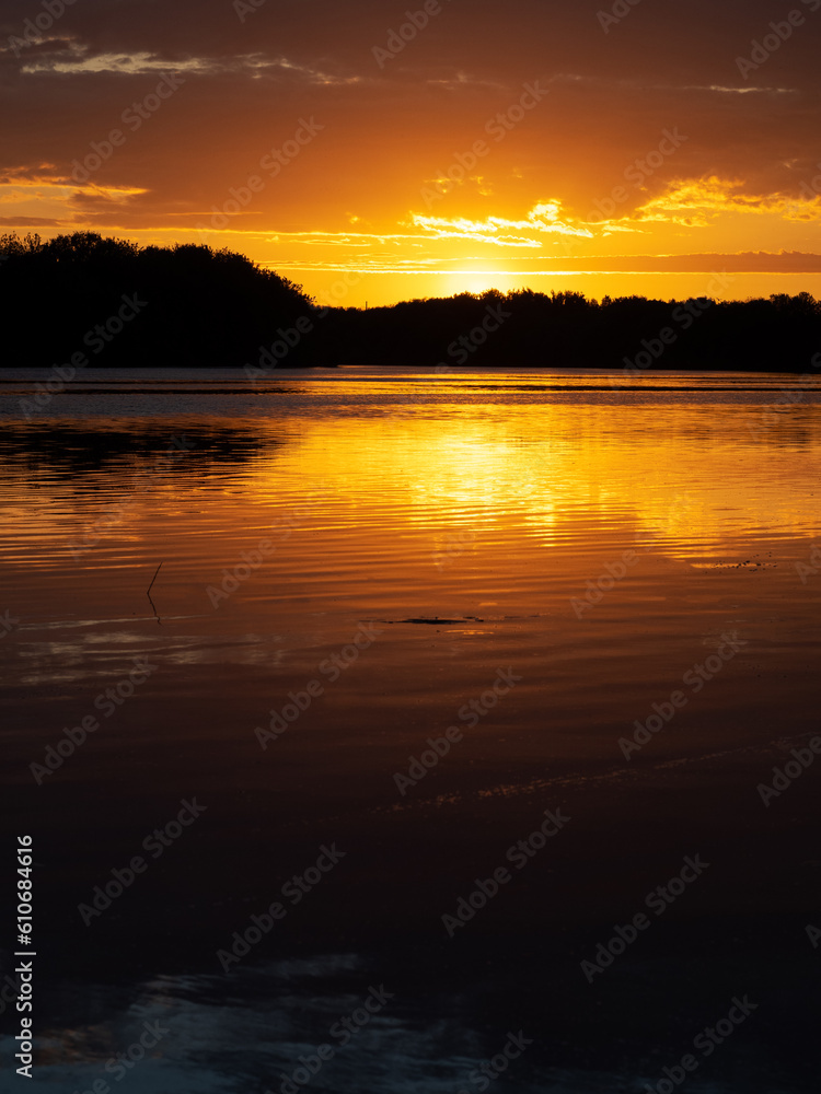 Colorful sunset over the river, reflection in the water. Tree silhouettes, vertical photo