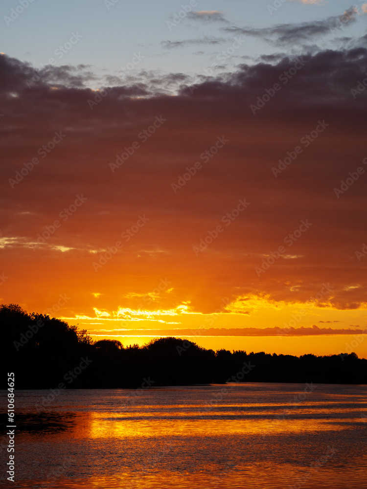 Colorful sunset over the river, reflection in the water. Tree silhouettes, vertical photo
