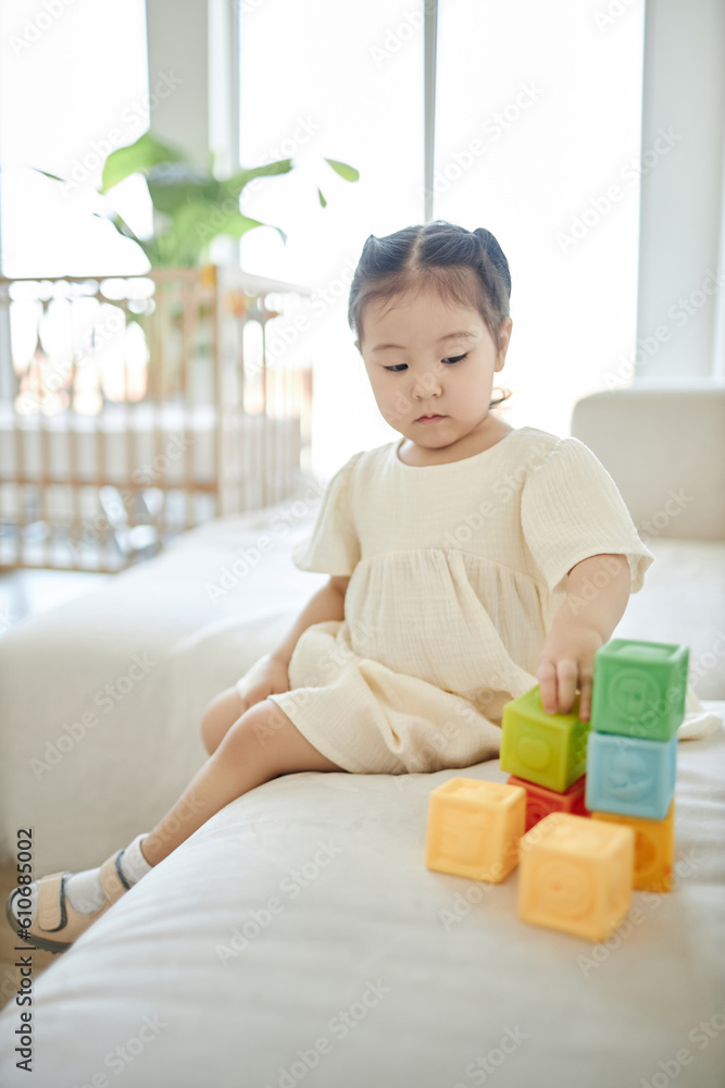 Cute little girl building tower from blocks while sitting on sofa in the living room Cute little girl building tower from blocks while sitting on sofa in the living room