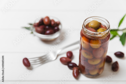 Olives in a glass jar on a white wooden background. pitted green olives in jar.Pickled olives in glass jar. On a wooden background.Marinaded olives. Space for text.Space for copy. Vegan food.