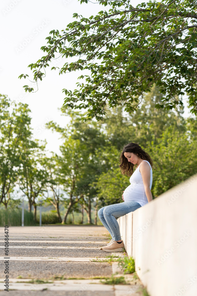 Naklejka premium Young pregnant woman looking her belly sitting in the street
