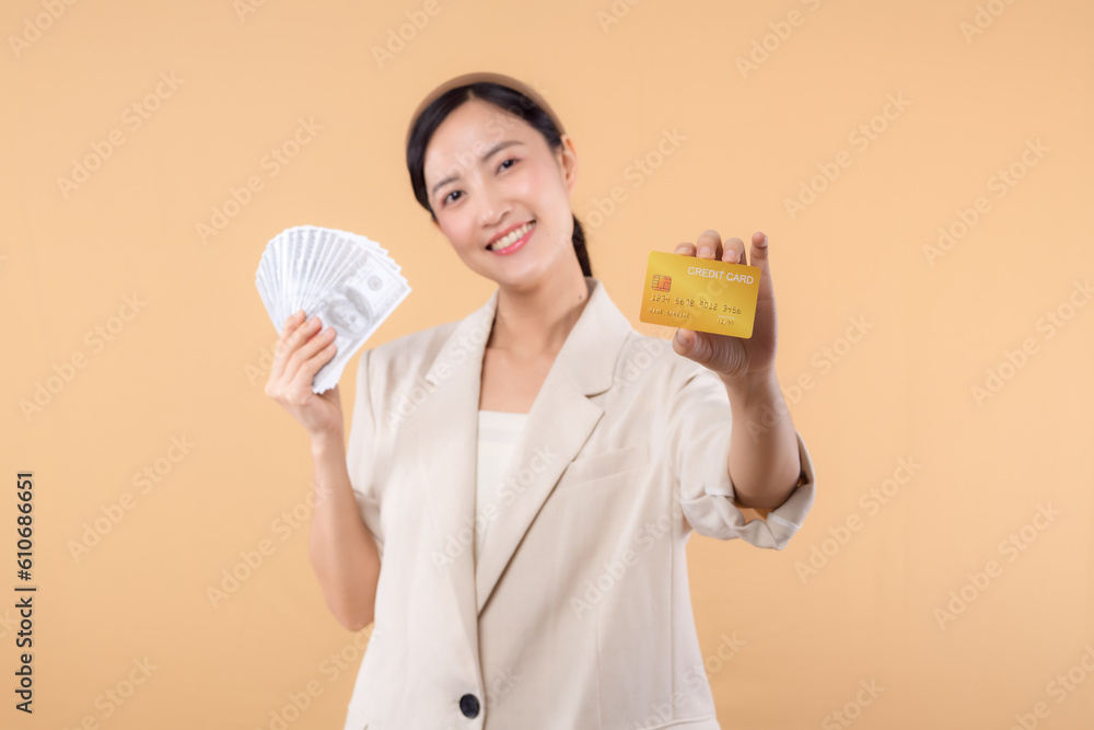 portrait of happy successful confident young asian business woman wearing white jacket holding cash money dollars and credit card standing over beige background. millionaire business, shopping concept portrait of happy successful confident young asian business woman wearing white jacket holding cash money dollars and credit card standing over beige background. millionaire business, shopping concept